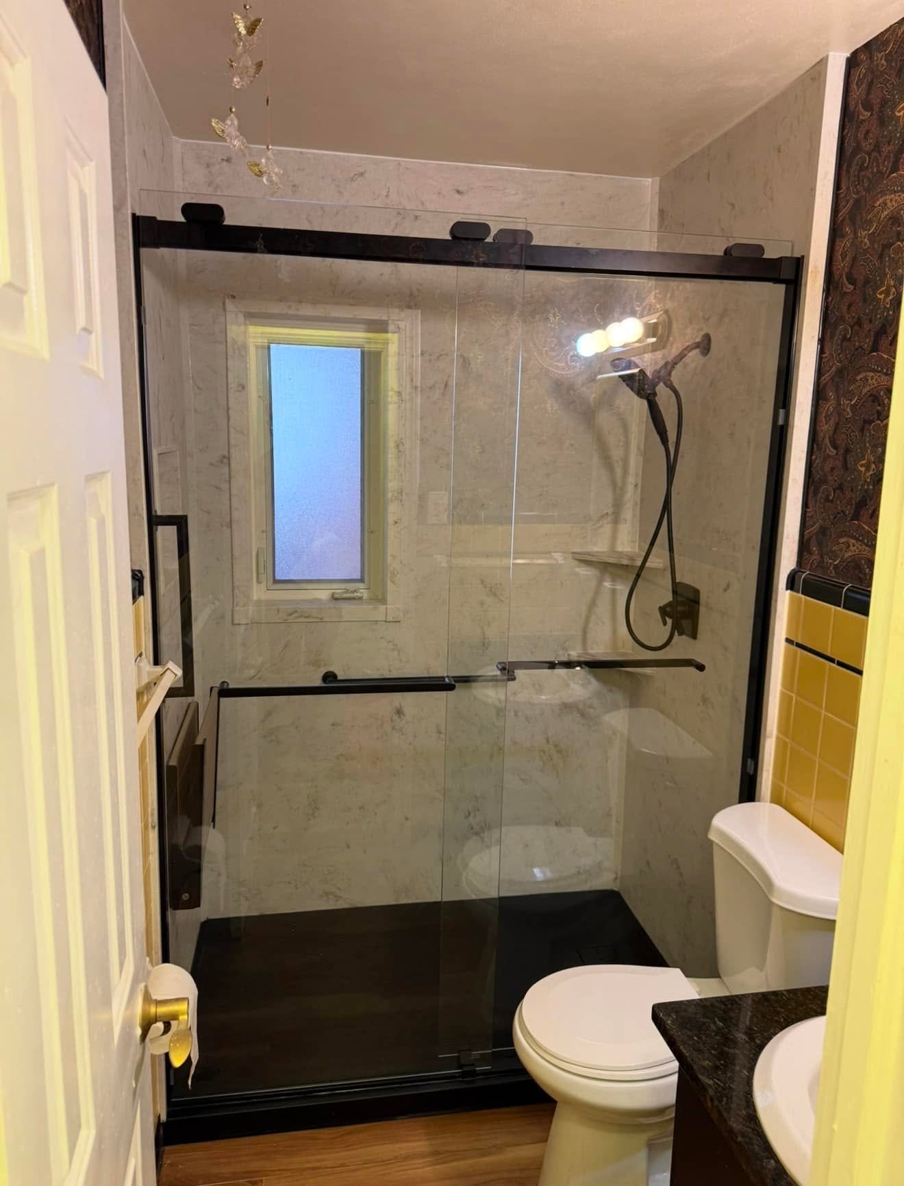 After: a walk-in shower with a glass panel, fold-down seat, grab bar and handheld shower